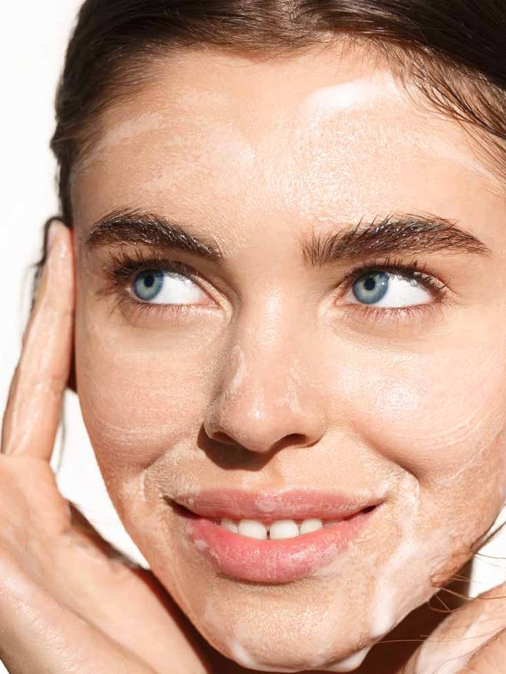 A woman smiling with gel cleanser worked over her face