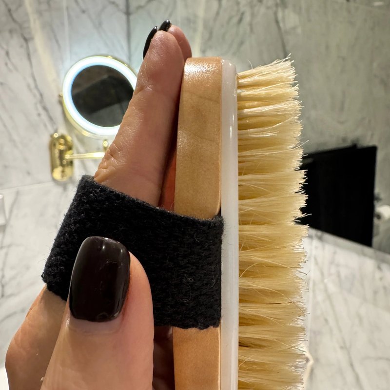 The FoYL Body Brush strapped across a hand in a marble bathroom